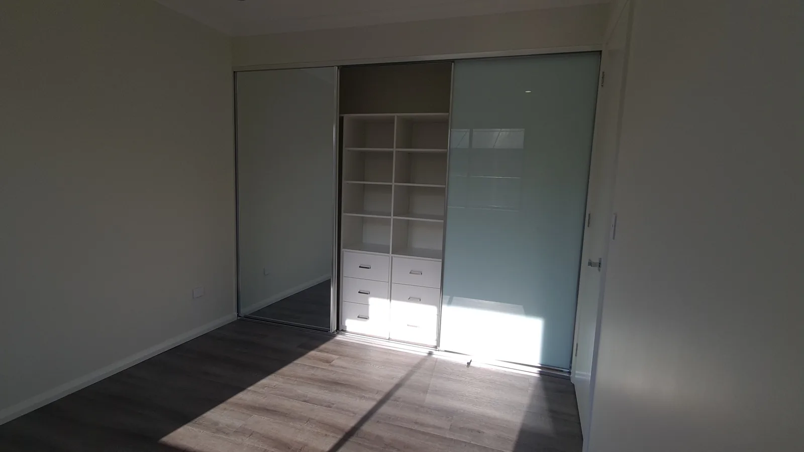 Bedroom with mirrored sliding wardrobe doors revealing fitted shelves and drawers.