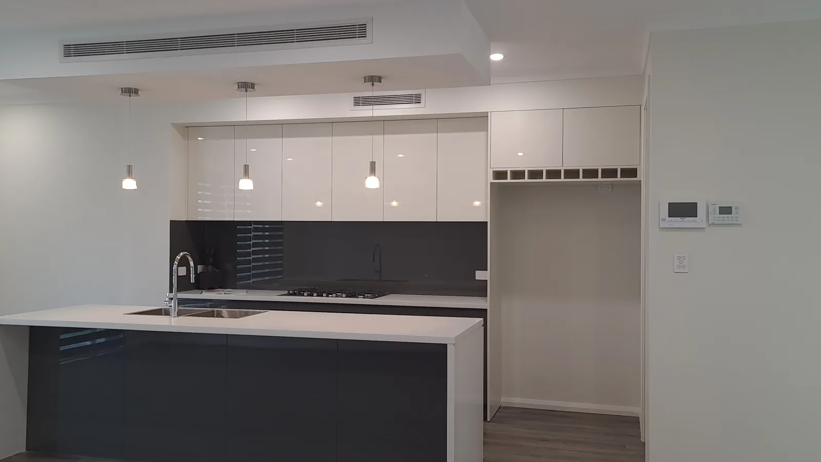 Contemporary kitchen with a long island, double-bowl sink, gloss cabinetry, black glass splashback and pendant lights.