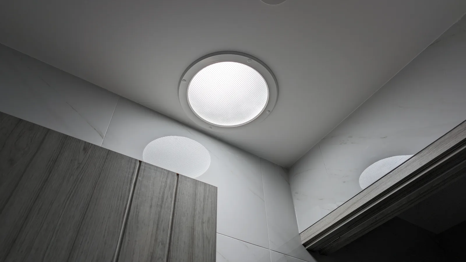 Round tubular skylight diffuser in a laundry ceiling above tiled walls and timber-look cabinetry.