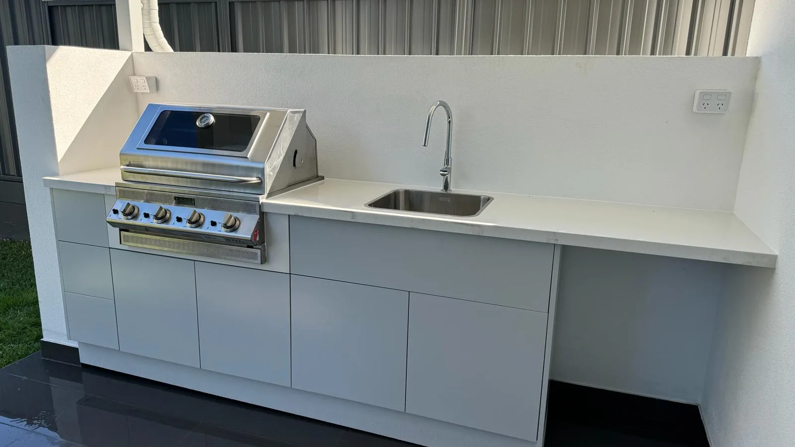Outdoor kitchen with a built-in barbecue, stainless-steel sink, benchtop and fitted cabinetry.