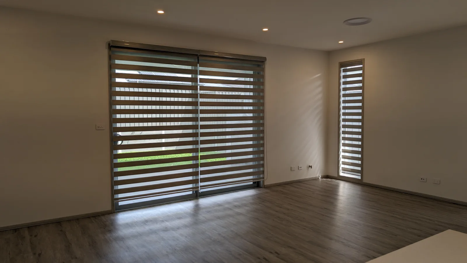 Living area with zebra blinds across wide sliding doors and hybrid flooring.